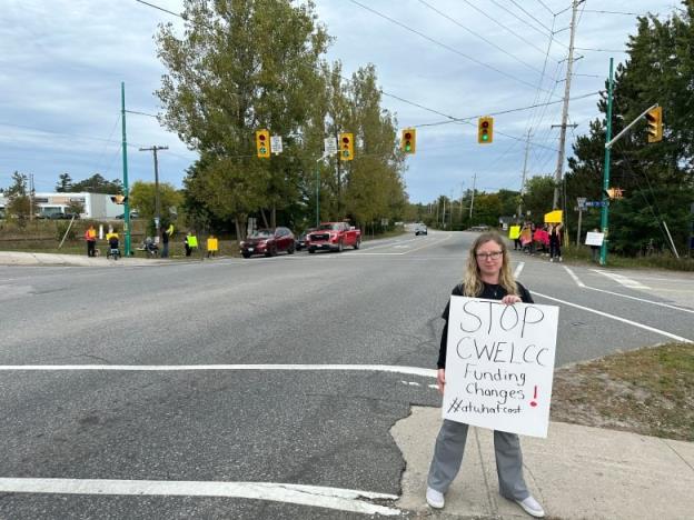 Anya Kerr standing in next to an intersection holding a sign that says