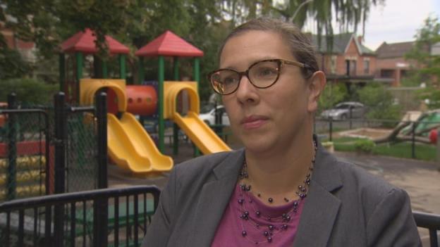 Carolyn Ferns, wearing a gray blazer and glasses, standing near a children's playground